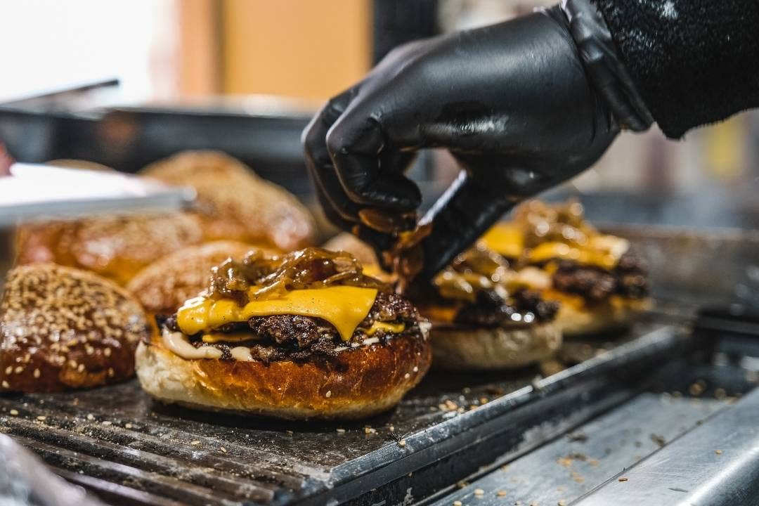 Chef preparing gourmet cheeseburgers with caramelized onions in a restaurant kitchen