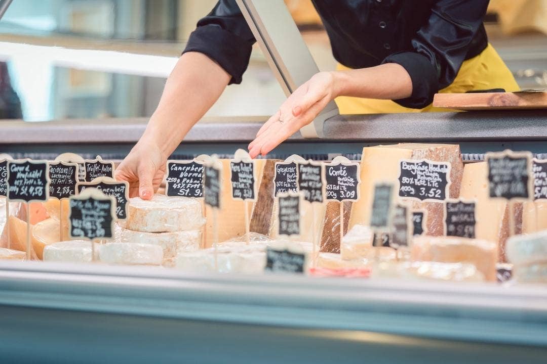 Deli worker organizing cheese selection in refrigerated display case