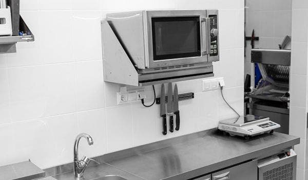 Commercial kitchen countertop with a mounted microwave, knives, and stainless steel work area.