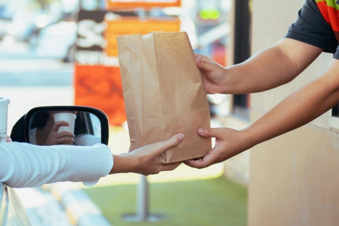 Drive-thru staff handing takeout bag to customer in car