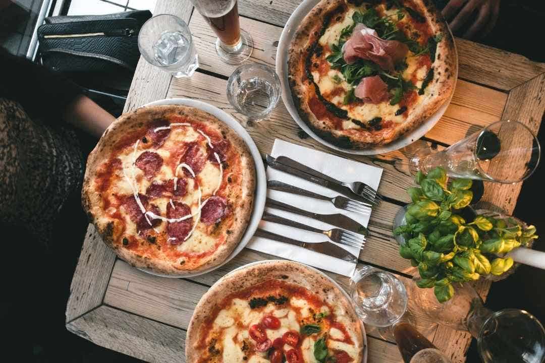 Tabletop view of assorted wood-fired pizzas with drinks and utensils.