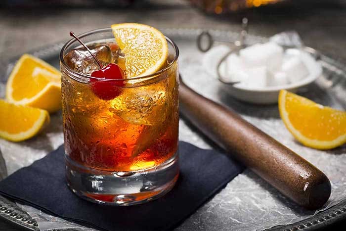 tasty alcoholic old fashioned cocktail with orange slice, cherry, and lemon peel garnish
