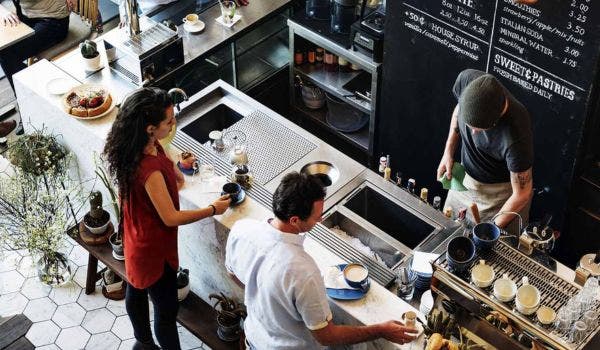 Overhead view of a coffee shop counter with baristas preparing drinks for customers.