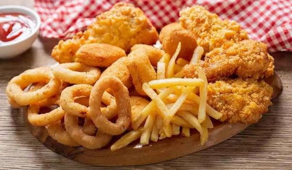 Wooden platter with a variety of fried foods, including onion rings, fries, and chicken.