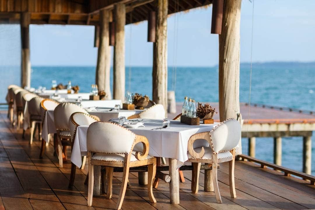 Oceanfront hotel patio dining setup with wooden chairs and white tablecloths