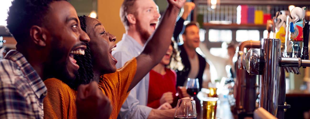 Group Of Excited Customers In Sports Bar Watching Sporting Event On Television
