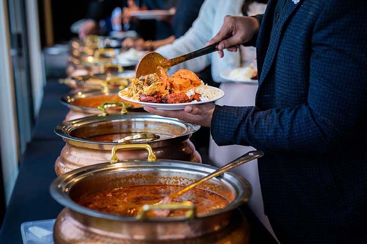 Man puts Indian food on a plate at a restaurant buffet.