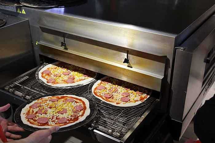 three pizzas move along a conveyor belt into an electronic baking oven