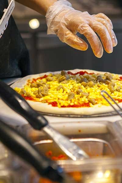 A pizza is made on a cutting board of a pizza prep table.
