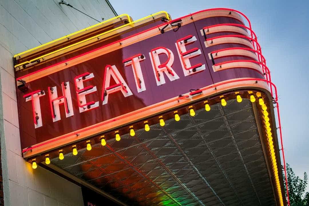 Vintage theater sign lit with neon lights against a blue evening sky