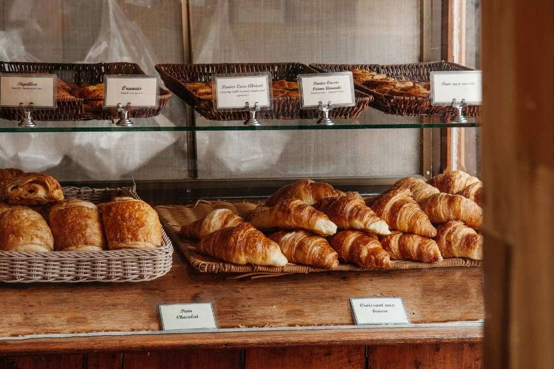 Bakery case filled with croissants and pastries in wicker baskets and glass shelves.