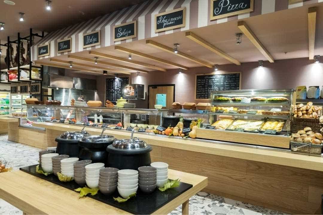 Modern cafeteria with food stations, soup warmers, and fresh bakery items on display.