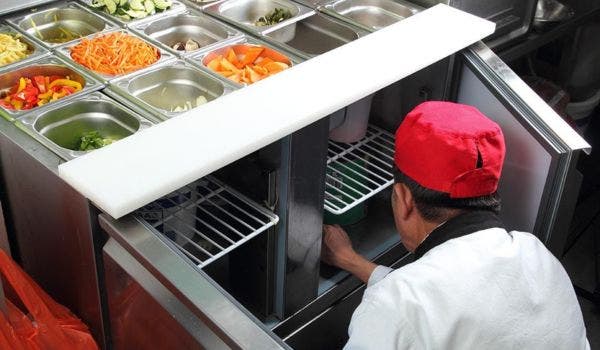 Chef preparing ingredients from a prep table with fresh vegetables in a commercial kitchen.