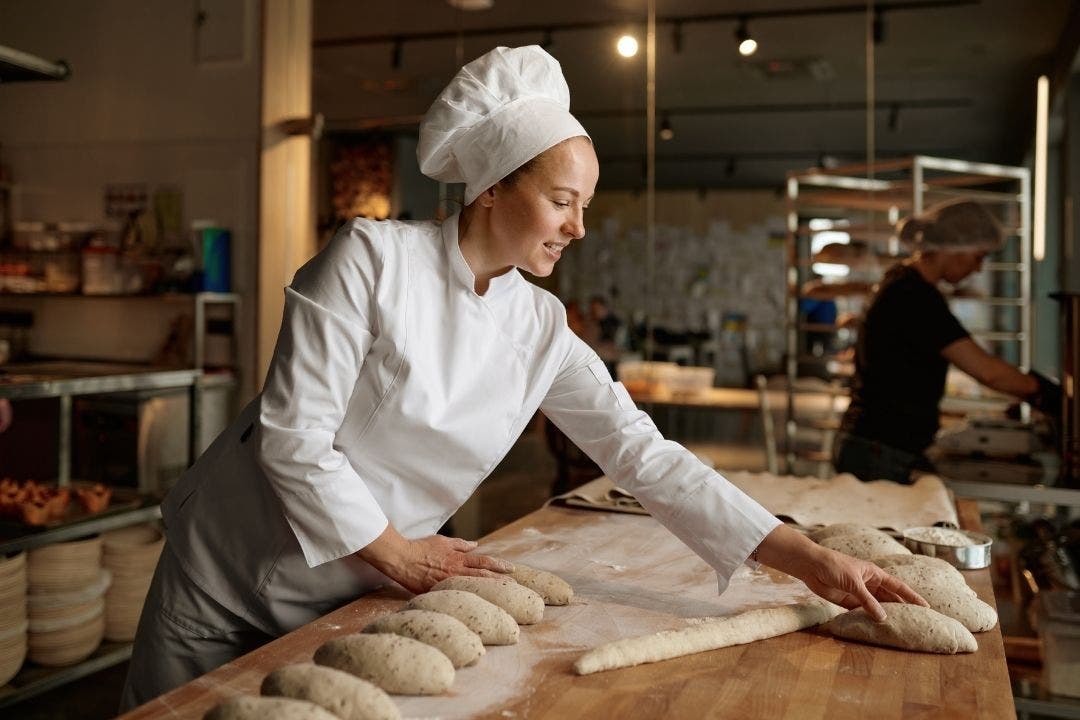 Female baker shaping bread dough in commercial bakery