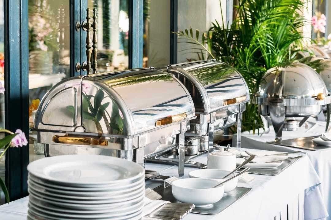 Catering buffet with chafing dishes, plates, and serving utensils