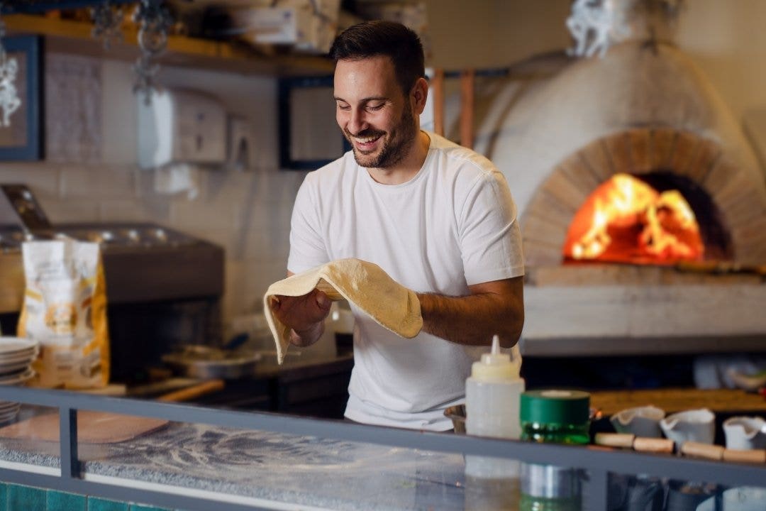 Smiling chef preparing pizza dough near wood-fired oven
