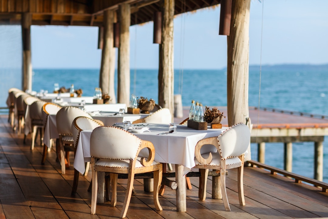 Waterfront resort restaurant with elegant dining tables set by the ocean.