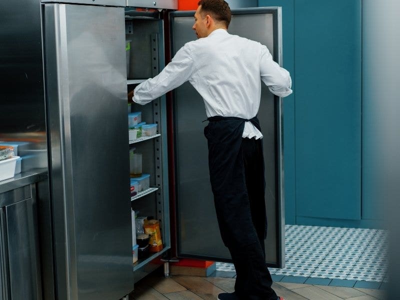 Male chef reaching into a refrigerator in a commercial kitchen.