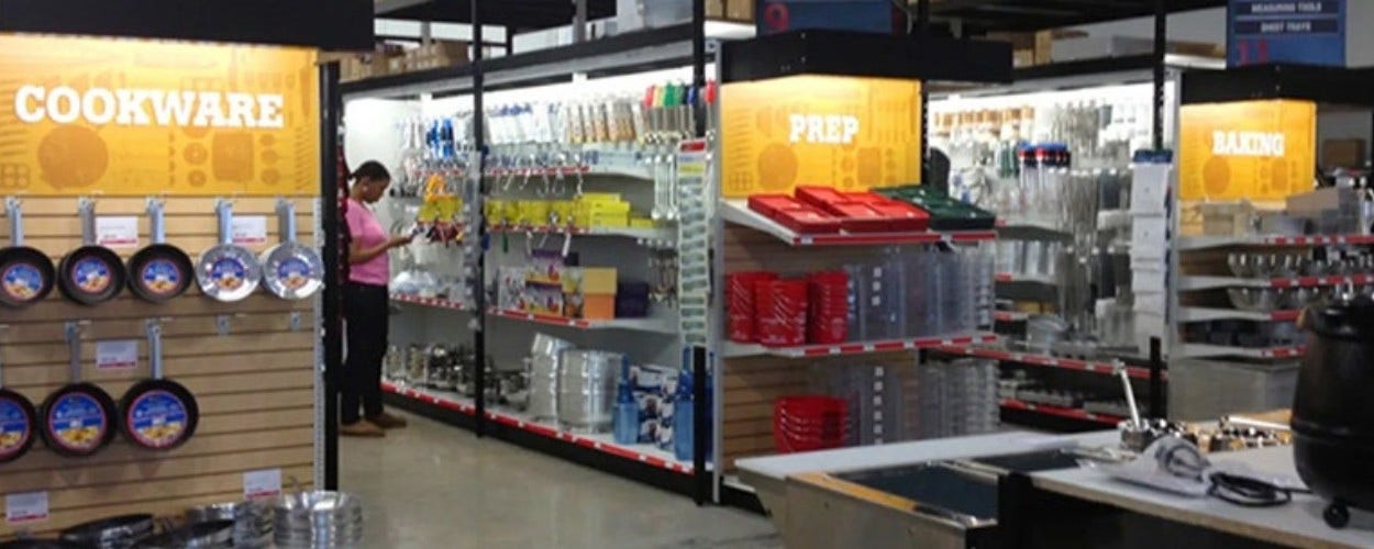 Women in a pink shirt standing inside a Restaurant Equippers store browsing for kitchen products and accessories
