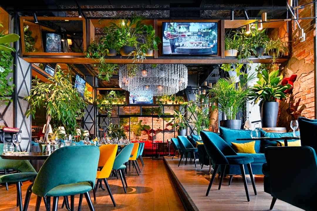 Restaurant interior – Colorful upscale restaurant with greenery, chandeliers, and elegant seating.