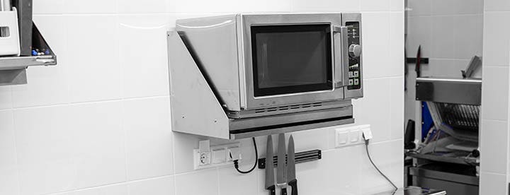 The working area of a commercial kitchen including a microwave on a microwave shelf.