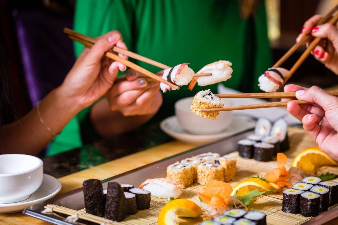 Chopsticks picking sushi from assorted platter at Asian restaurant table