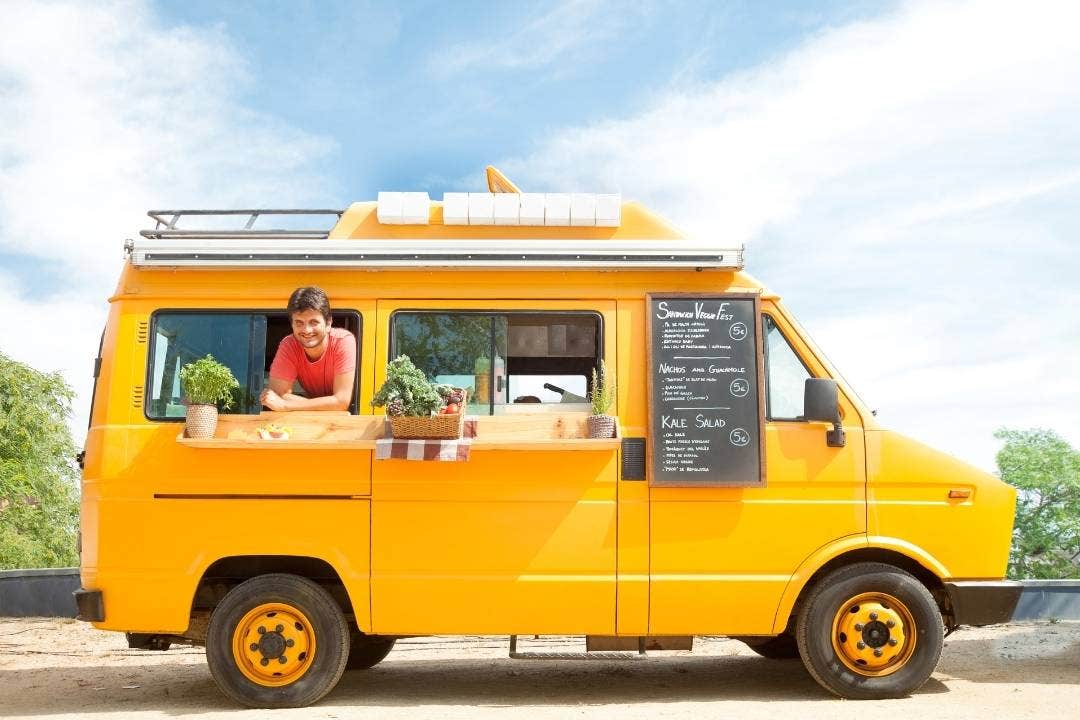 Smiling vendor inside bright yellow food truck with menu board and herb display