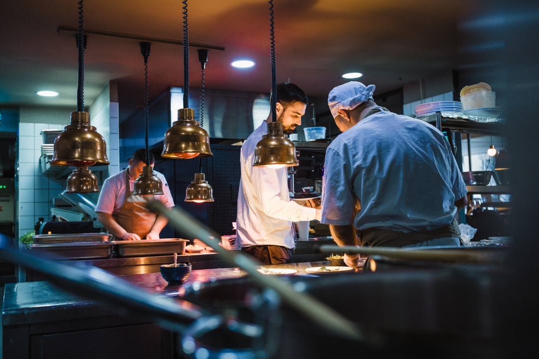 Busy commercial kitchen with chefs plating food under heat lamps