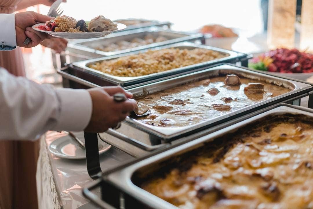Buffet line with guests serving hot dishes from chafing pans at a catered event.