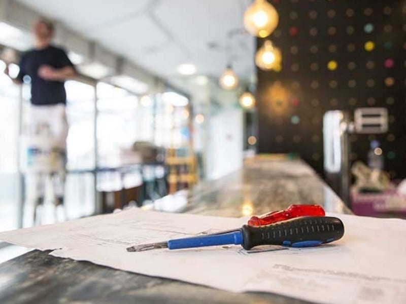 Construction going on in a restaurant building showing a man standing on a ladder, plans, and screwdrivers.