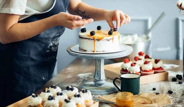 Pastry chef decorating a cake with fresh berries and caramel drizzle.