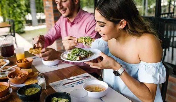 oung woman enjoying authentic Mexican food with friends at a restaurant, featuring guacamole and other traditional dishes.