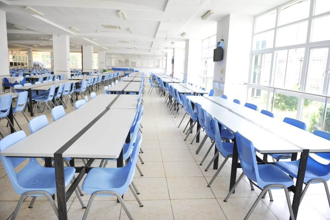 Empty school cafeteria with blue chairs and long white tables