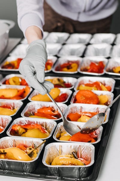 Chef protioning out meals in aluminum square tins with spoons.