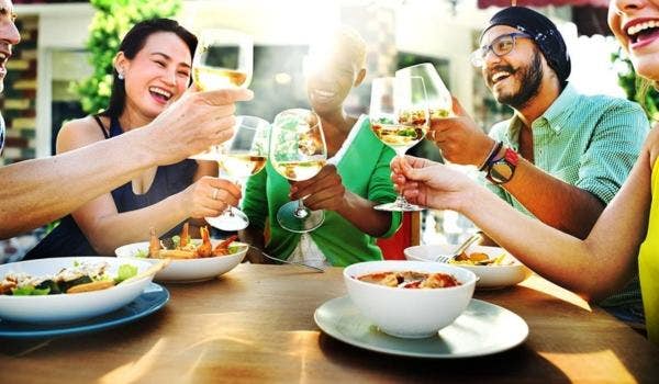 Group of friends celebrating at a lively bar with beers, wine, and cheers.