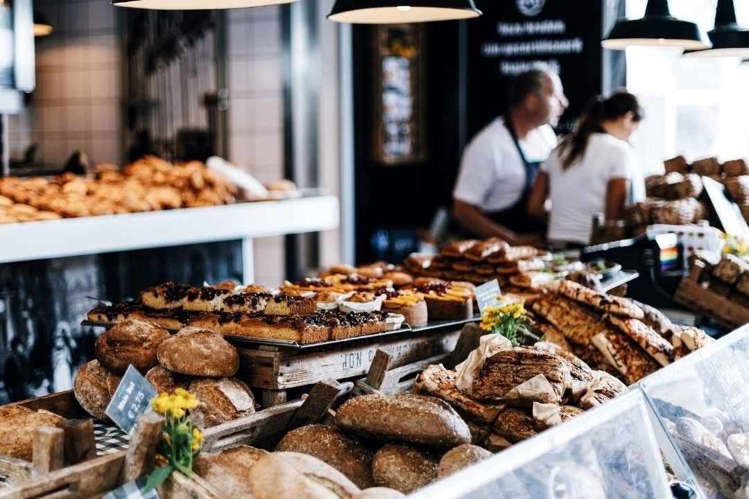 Fresh bread and pastries displayed in a busy artisan bakery with staff in the background
