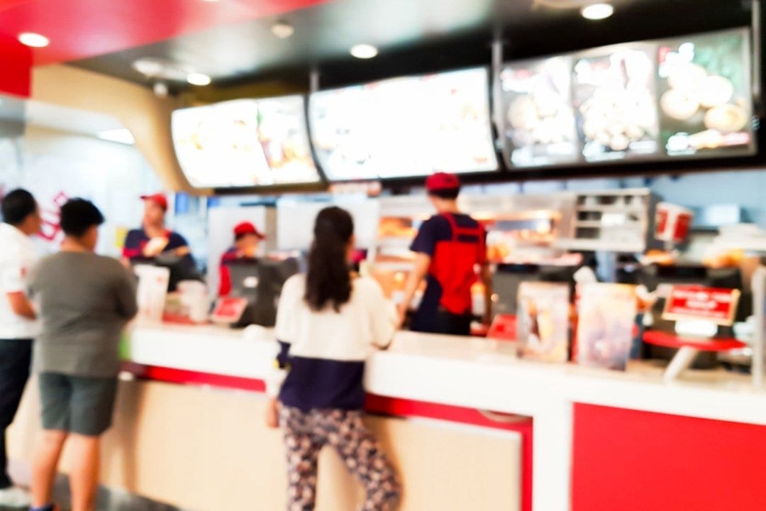Customers ordering food at a busy fast food counter with menu boards overhead