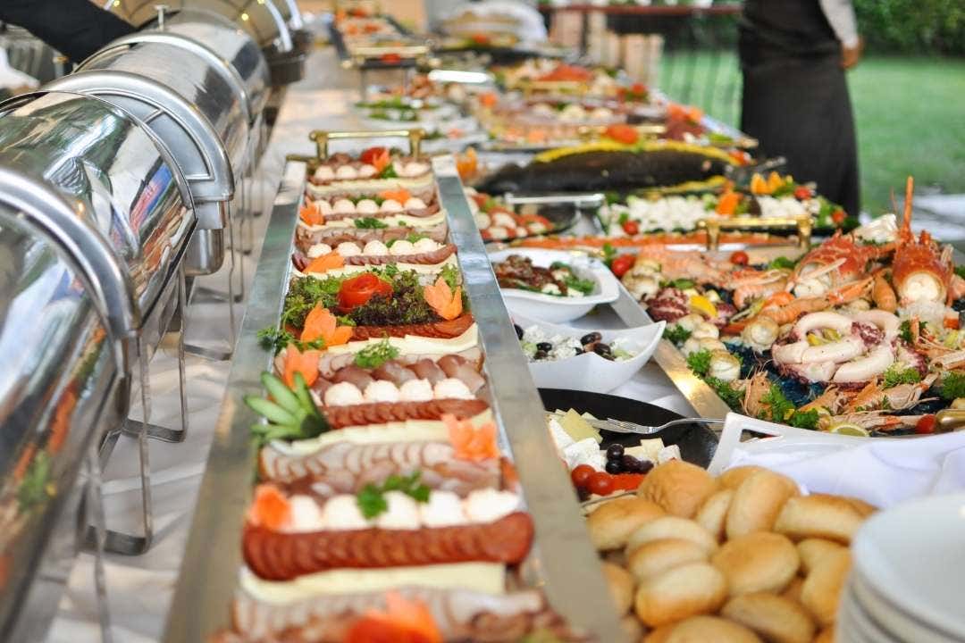 Catering event with sliced vegetables and deli meats displayed in buffet trays