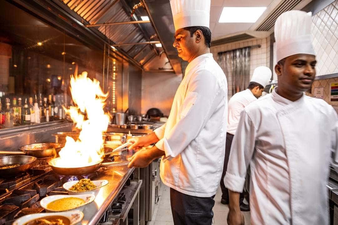 Chef cooking with flames in busy commercial kitchen using vegetable cutter prep