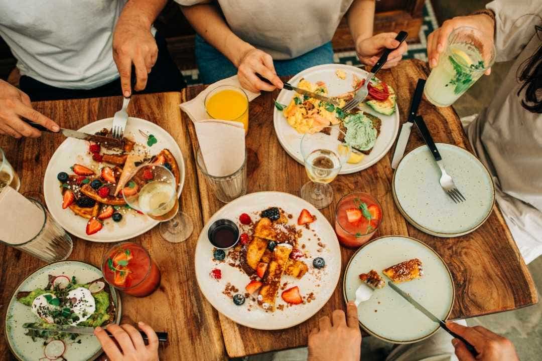 Friends enjoying brunch with waffles, eggs, and juice at a cozy cafe table