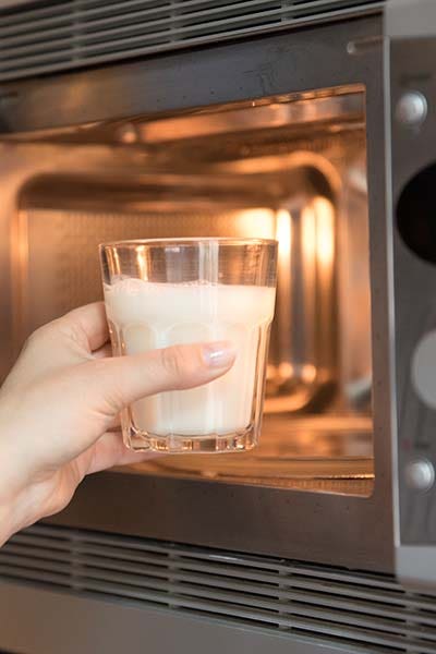 Woman warming a glass of milk in the microwave