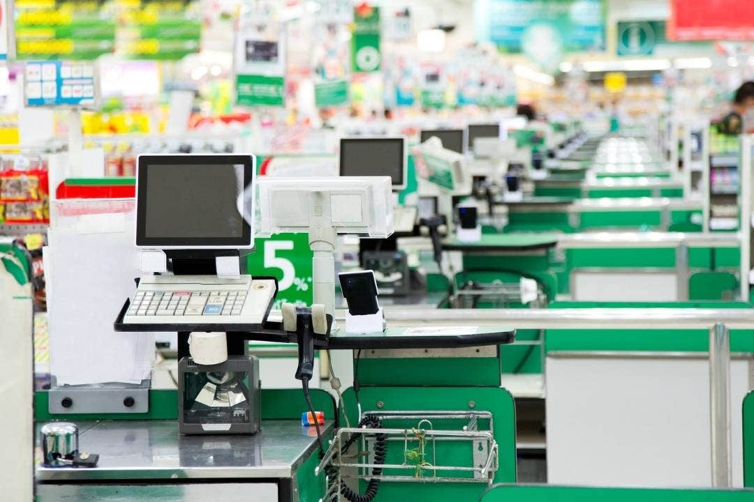 Empty green checkout lanes in a brightly lit grocery store.